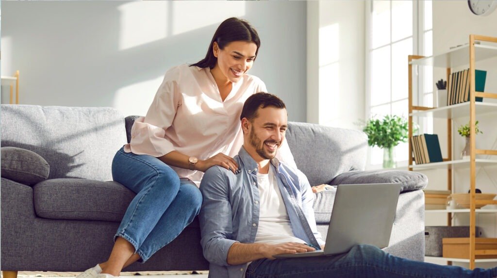 Young married couple sitting on sofa in the living room at home using tablet PC