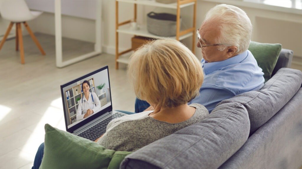 Senior couple sitting on couch with laptop and having video call with online doctor