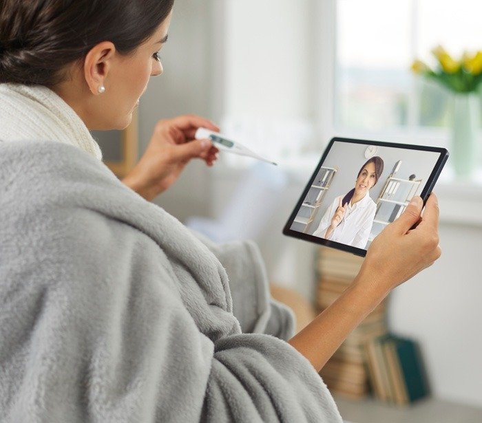 Sick young woman is using digital tablet device, having online telemedicine consultation, holding thermometer