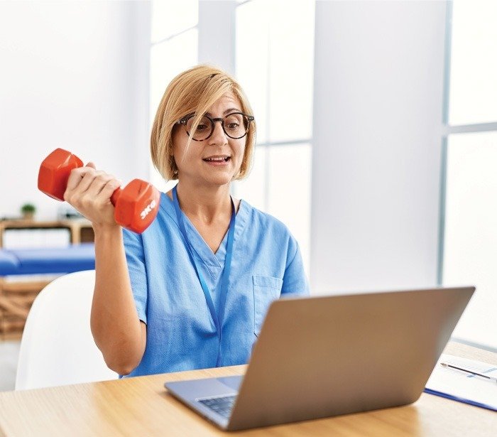 woman wearing physio therapy uniform doing tele rehab using dumbbells